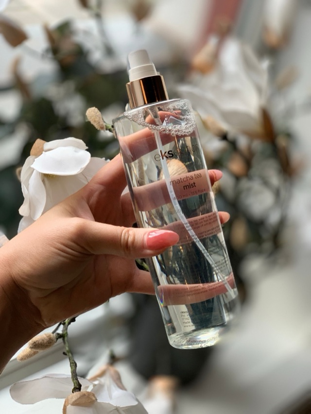 Hand holding a body mist spray bottle among white flowers